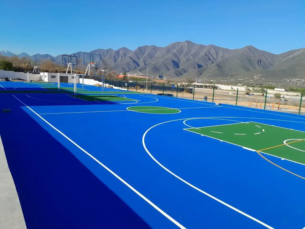 Cancha de básquetbol pintada en azul y verde, con montañas al fondo