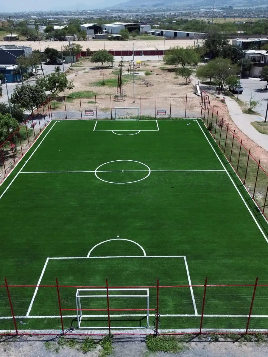 Vista desde arriba de una cancha de fútbol con pasto sintético, cerca y malla
